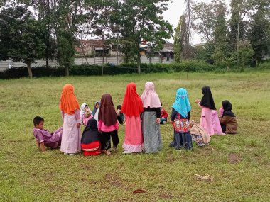 Doğadaki okul aktiviteleri. Bir grup çocuk ve öğretmen. Erkekler ve kızlar oyun oynarken yeşil çimlerin üzerinde birlikte oturuyorlar. Bandung-West Java, 21 Mart 2023
