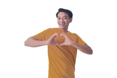 Sevgiyle gülümseyen yakışıklı Asyalı adam elleriyle kalp sembolü yapıyor. Romantik kavram. Aşk emojisi olan Endonezyalı bir adam. Genç Asyalı adam mutlu hissediyor ve romantik şekiller kalp hareketlerini ifade ediyor..