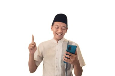 Asyalı Müslüman bir adam akıllı bir telefon tutuyor, Happy internetten özel bir hediye alıyor, mutlu Asyalı Müslüman adam cep telefonunu tutuyor ve işaret ediyor. Ramazan konsepti. Şaşırdım.