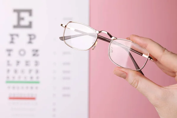 Γυαλιά Διόρθωσης Όρασης Στο Χέρι Στο Φόντο Ενός Πίνακα Δοκιμής — Φωτογραφία Αρχείου