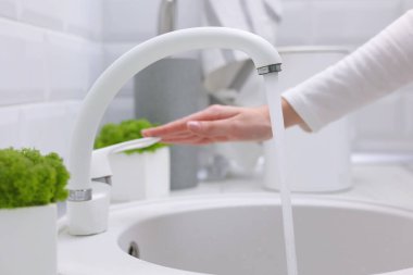 Bir kız modern bir iç mekanda mutfaktaki musluğun suyunu açar. Saf su, hijyen. Yüksek kalite fotoğraf