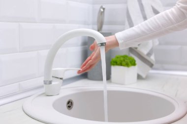 Bir kız modern bir iç mekanda mutfaktaki musluğun suyunu açar. Saf su, hijyen. Yüksek kalite fotoğraf