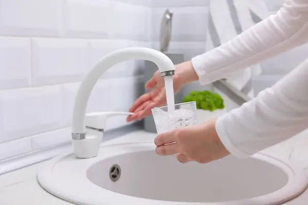 Bir kız mutfak musluğundan bardağa temiz su döker. Saf su. Yüksek kalite fotoğraf