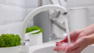 Bir kız, mutfağın parlak bir bölümündeki musluktan eline temiz su çeker. Yüksek kalite 4k görüntü