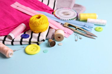 Sarı zemin üzerinde iplikler, düğmeler ve makas da dahil olmak üzere çeşitli dikiş araçlarının ve malzemelerin üst görünümü.
