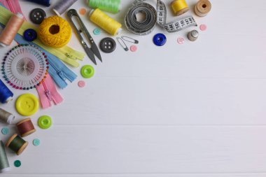 Sarı zemin üzerinde iplikler, düğmeler ve makas da dahil olmak üzere çeşitli dikiş araçlarının ve malzemelerin üst görünümü.