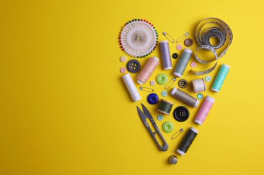 Sarı zemin üzerinde iplikler, düğmeler ve makas da dahil olmak üzere çeşitli dikiş araçlarının ve malzemelerin üst görünümü.