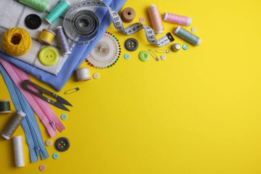 Sarı zemin üzerinde iplikler, düğmeler ve makas da dahil olmak üzere çeşitli dikiş araçlarının ve malzemelerin üst görünümü.