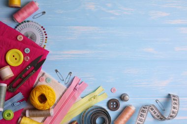 Sarı zemin üzerinde iplikler, düğmeler ve makas da dahil olmak üzere çeşitli dikiş araçlarının ve malzemelerin üst görünümü.