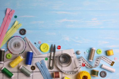 Sarı zemin üzerinde iplikler, düğmeler ve makas da dahil olmak üzere çeşitli dikiş araçlarının ve malzemelerin üst görünümü.