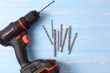 Üzerinde çeşitli matkap uçları bulunan kablosuz matkap mavi ahşap bir yüzeye yerleştirilir. DIY projeleri için mükemmel.