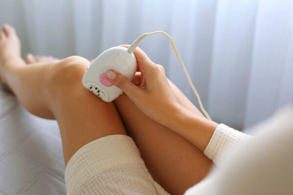 A girl removes unwanted body hair with a modern mechanical epilator in the interior of a room. High quality 4k footage