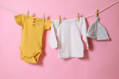 Bebek kıyafetlerinin ve sevimli aksesuarların canlı ve renkli bir görüntüsü hoş pembe bir arka planda kuruyor.