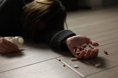 Halıya dağılmış haplarla potansiyel bir aşırı dozu tasvir eden dramatik bir sahne umutsuzluğu simgeliyor.