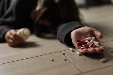 Halıya dağılmış haplarla potansiyel bir aşırı dozu tasvir eden dramatik bir sahne umutsuzluğu simgeliyor.