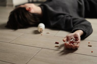 Halıya dağılmış haplarla potansiyel bir aşırı dozu tasvir eden dramatik bir sahne umutsuzluğu simgeliyor.