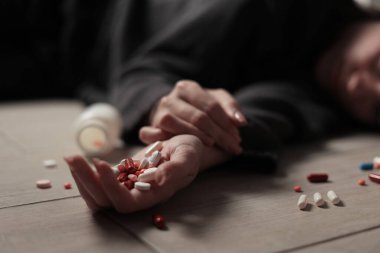 Halıya dağılmış haplarla potansiyel bir aşırı dozu tasvir eden dramatik bir sahne umutsuzluğu simgeliyor.