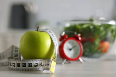 Canlı yeşil bir elma, bir mezura ve bir kase renkli salata sağlıklı bir yaşam tarzını simgeler.