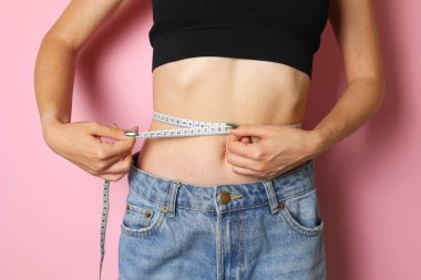 Kendine güvenen bir kadın, parlak sarı bir arka planda duran bir mezura kullanarak belini ölçer.