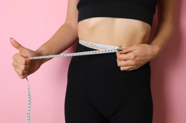 Kendine güvenen bir kadın, parlak sarı bir arka planda duran bir mezura kullanarak belini ölçer.