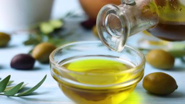 Gümüş bir kaşık altın zeytin yağını taze zeytin ve canlı yeşil yapraklarla çevrili bir kaseye serpiştirir.