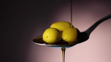 Gümüş bir kaşık altın zeytin yağını taze zeytin ve canlı yeşil yapraklarla çevrili bir kaseye serpiştirir.