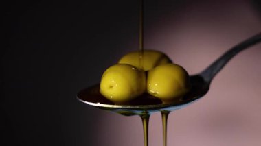 Gümüş bir kaşık altın zeytin yağını taze zeytin ve canlı yeşil yapraklarla çevrili bir kaseye serpiştirir.