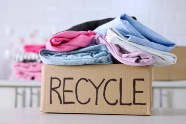 Giysilerle dolu renkli bir kutu, açıkça Geri Dönüşüm etiketi ile, sürdürülebilir ve eko-dostça moda tercihlerini destekliyor