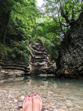 Dişi güzel kırmızı pedikür ayakları, arka plandaki kayalıklarda, dağ deresinin berrak suyunda ferahlatıcı. Yüksek kalite fotoğraf