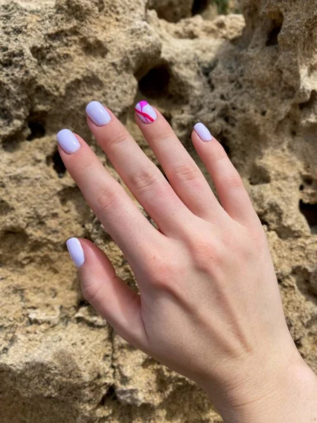 Female hand nails with a beautiful light pink manicure on a caves background, square shape nails. High quality photo