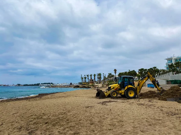 Kumsaldaki traktör bir çukur kazıyor, buldozer mavi denizin yanındaki sahilde çalışıyor, yan görüş. Yüksek kalite fotoğraf