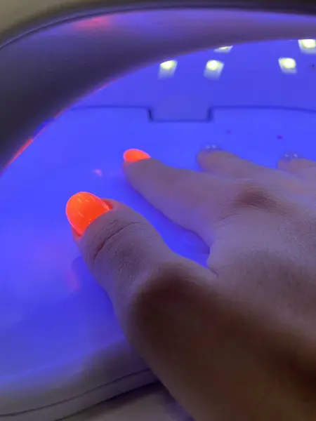 Female hand with neon orange manicure inside a blue UV lamp, drying gel polish. Manicure process, drying stage. High quality photo