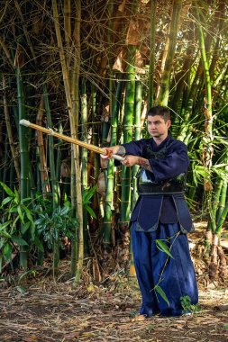 Ormanda bambu kılıçlı geleneksel kendo üniformalı adam.