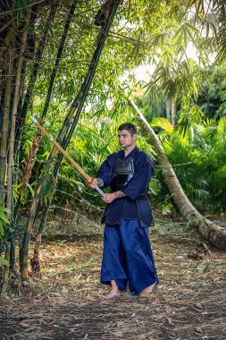 Man in traditional kendo uniform with bamboo sword in the jungle clipart