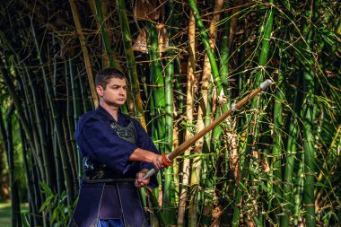 Ormanda bambu kılıçlı geleneksel kendo üniformalı adam.