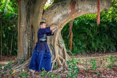 Man in traditional kendo uniform with bamboo sword in the jungle clipart