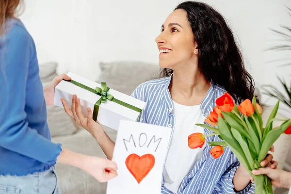 Mom is happy to receive an unexpected gift from her children. Children give their mother a bouquet of tulips, a handmade card and a surprise box.