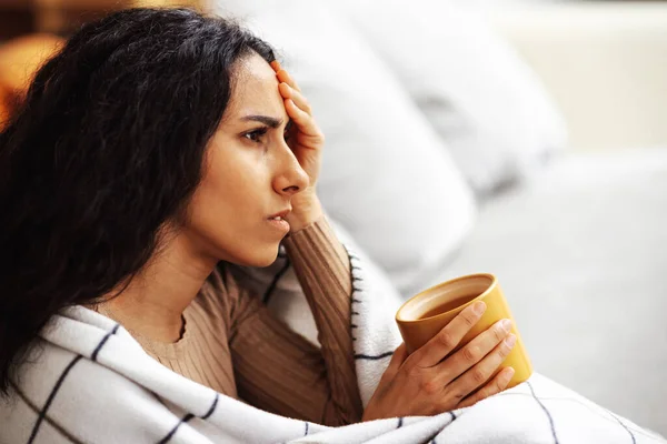 Arap 'ın genç ve güzel kadını bir elinde battaniyeye sarılı gri bir kanepede oturuyor, diğer elinde de kafasını tutan bir bardak tutuyor. Stres ve depresyonla başa çıkan kadın.