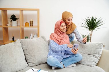İki güzel Arap kadını akıllı telefonlarına bakar ve haberleri paylaşır. Kadın alışveriş sitesi buldu. Evde online alışveriş konsepti. Türbanlı kızların hoş, sade bir atmosferi vardır.