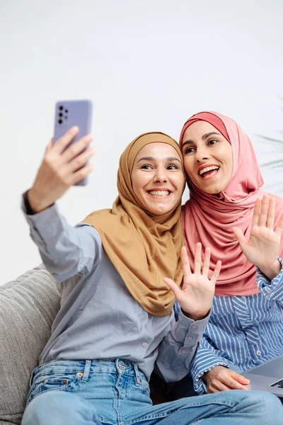 stock image Two muslim woman wear hijabi taking video calling with smartphone, ramadan celebration concept. Girls waving their hands at the screen smile and are happy to see their family. Vertical image