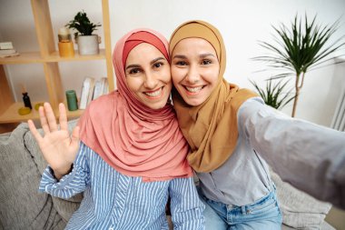 Türbanlı güzel Müslüman kadınlar evlerinden selfie çekip, uzayı kopyalıyorlar. Gülümseyen ortadoğulu genç kızlar video görüşmeleri yaparken sarılıyorlar, oturma odasında kanepede oturuyorlar.