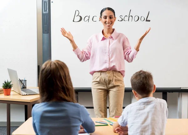 ハッピーダイバーズスクールの子供たちと教師の女性が学校の教室で机の上に立っている 現代教育と知識の概念 選択的なフォーカス 先生は子供たちに挨拶する — ストック写真