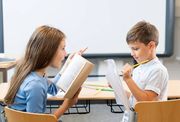 学校の子供たち 女の子と男の子が教室の机に座って活発な会話をする 少女はその本を少年に説明し 読み聞かせ 語った 興味と喜びで書くスクールボーイ — ストック写真
