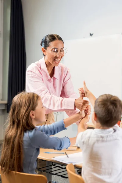 幸せな子供たちの垂直な傾向は 教室で教師と握手をしています 中東の若い教師と一緒に遊んでいる楽しい子供たち 遊びとクリエイティブラーニングのコンセプト — ストック写真