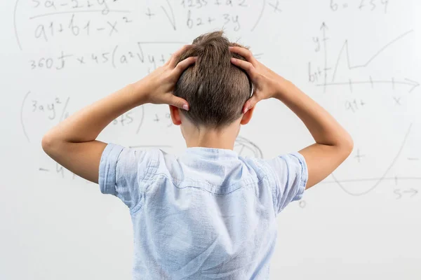黒板に反対するクラスに立っている学校のボーイの背中からの眺め 頭の上に手を握っている少年 ショックと感情的な小さな子供の肖像画 学校に戻る 数学の方程式を解くことができない — ストック写真