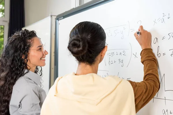 バックビュー 白いボードに立っている2人の若い女性学生が 例を書く方程式を解く 高校試験準備カレッジに入学しました 学習と教育の概念について — ストック写真