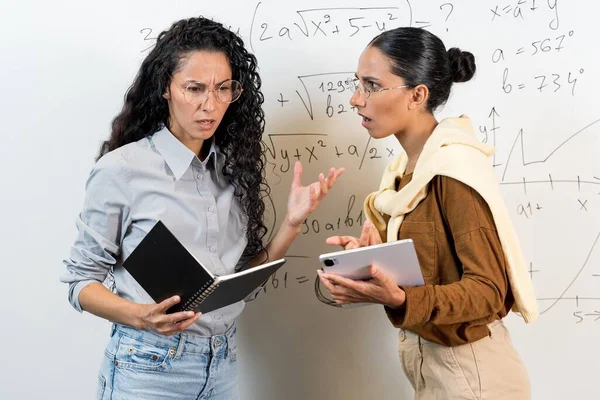 間違いと間違った答えのコンセプト 東洋の外観の2人の若い女性学生は数学の方程式を解決することはできません 彼らは困惑しています 彼らは教科書とタブレットを手に持っています — ストック写真