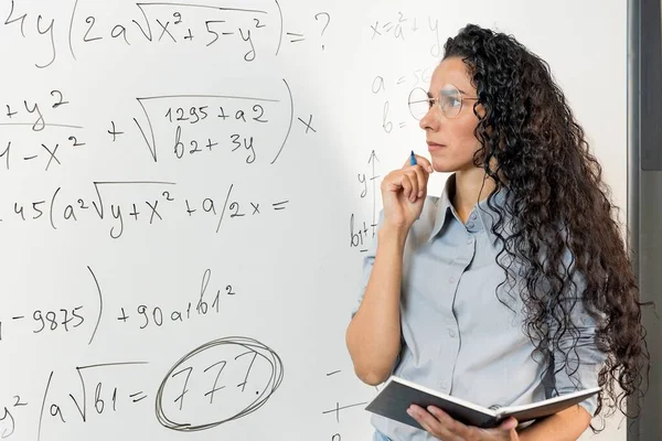 中東の若い女性教師は 教室で一人でプロジェクトに取り組んでおり 数学のタスクで魔女ボードを見て ノートを分析し ビジネスプロセスススケジュール 作業計画を考慮しました — ストック写真