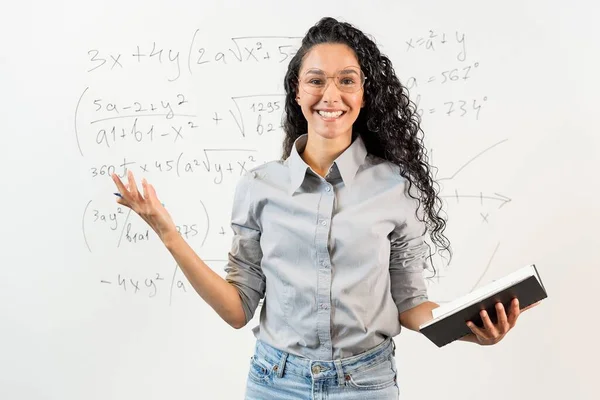 美しい東洋のカーリー髪の女性学生 数学のタスクで黒板の前に立っているチューターの肖像画 笑顔の女の子は彼女の手にノートを握っている聴衆に挨拶します — ストック写真