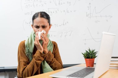 İş yerinde hasta çalışan genç Hintli bayan öğretmen, hapşıran işçilerin burnu akıyor ve alerjisi var, İspanyol iş yerinde dizüstü bilgisayarla masada oturuyor. Genç öğretmen karantina sırasında hastalanmış..